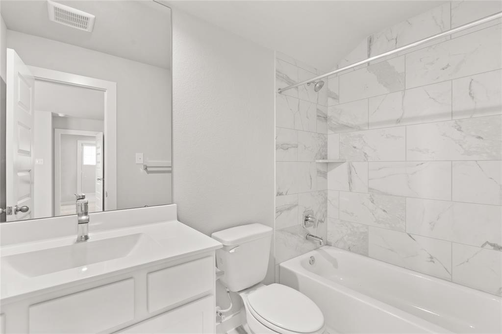 This private bath features tile flooring, bath/shower combo with tile surround, white stained wood cabinets, beautiful light countertops, mirror, dark, sleek fixtures and modern finishes.