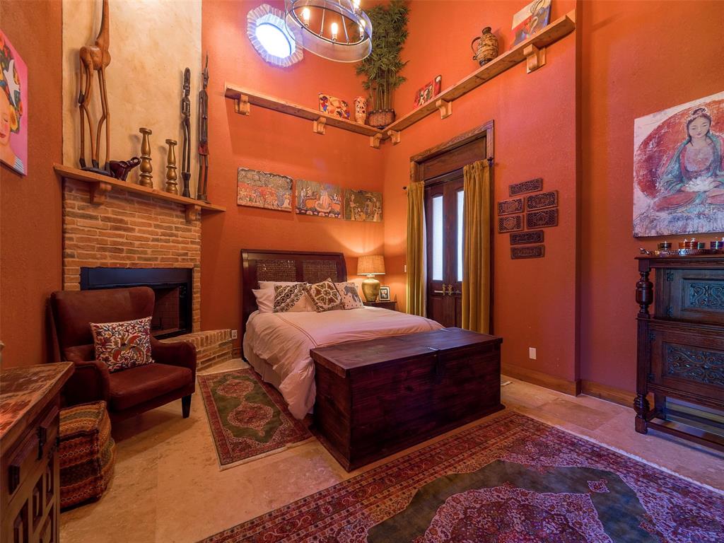 Bedroom in the downstairs primary suite with high ceilings and brick hearth around a wood burning fireplace.