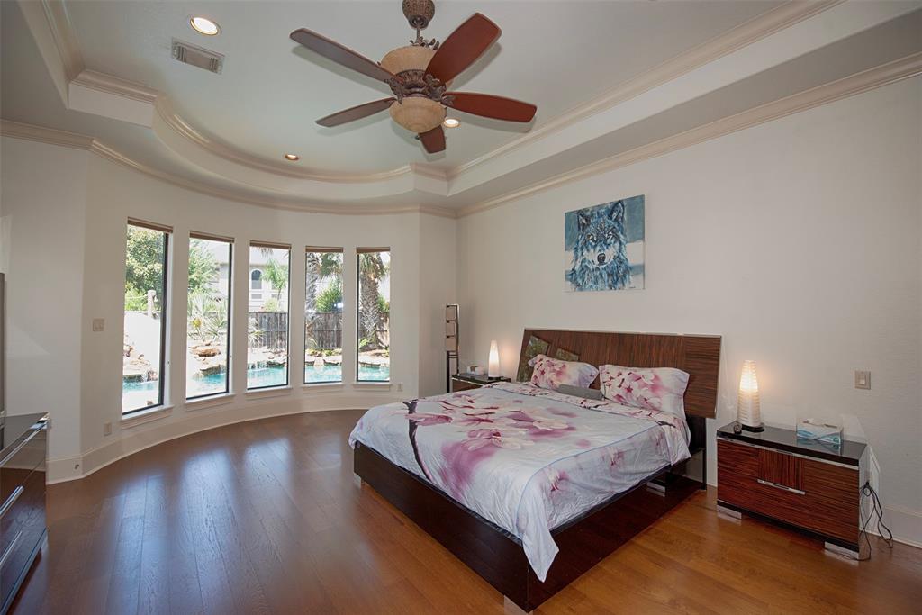 Expansive primary bedroom features tray ceiling, luxurious hardwood floors and curved wall of windows overlooking the pool.