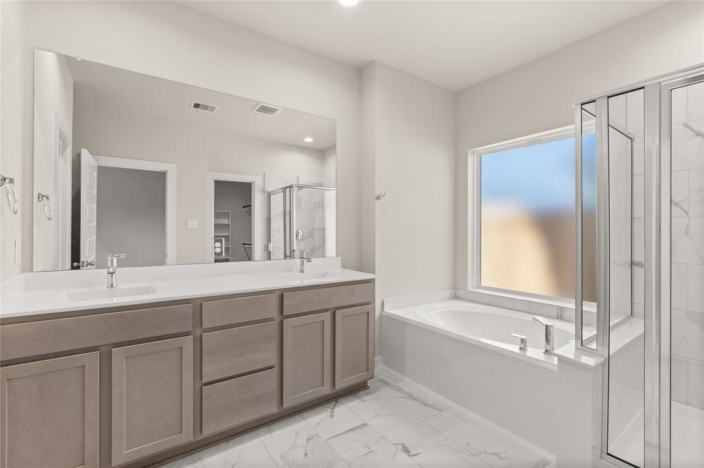 This primary bathroom is definitely move-in ready! Featuring a walk-in shower with tile surround, separate garden tub for soaking after a long day with custom tile detailing, light stained cabinets with light countertops, spacious walk-in closet with shelving, high ceilings, custom paint, sleek and dark modern finishes.