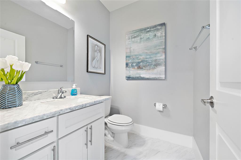 Find a convenient formal half bathroom for guests, fitted with a marble-topped vanity area, ample floor space, and plenty of cabinets with steel pulls.