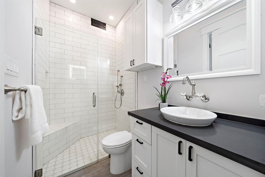 The secondary ensuite bath boasts a quartz vanity area with built-in cabinets plus a glass-enclosed shower with subway tile surround and tile floors.