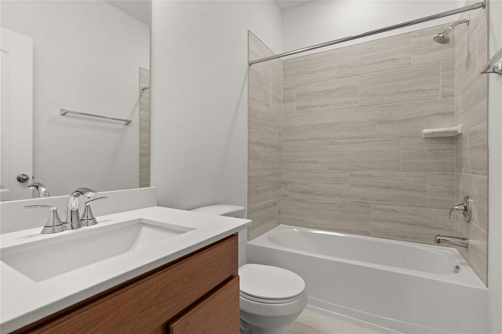 Secondary bath features tile flooring, bath/shower combo with tile surround, wood cabinets, beautiful light countertops, mirror, sleek fixtures and modern finishes!