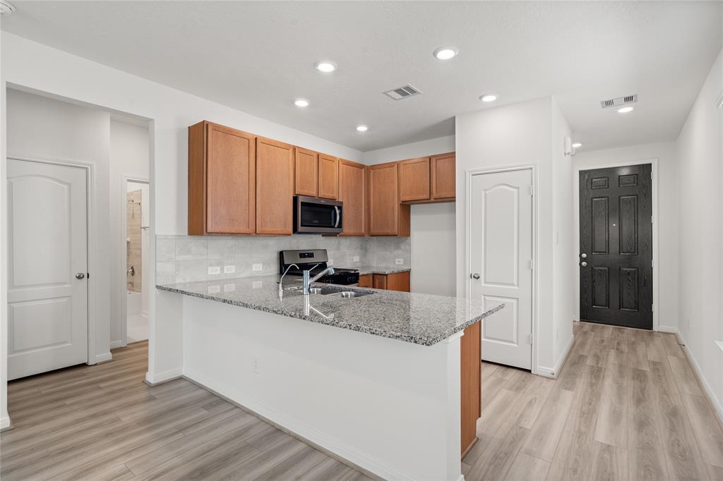 This stunning kitchen displays such a beautiful contrast with the wood stained cabinets, custom neutral paint, granite countertops, light modern backsplash, and SS appliances, kitchen island with extra storage, breakfast bar, recessed lighting, high ceilings and pantry.