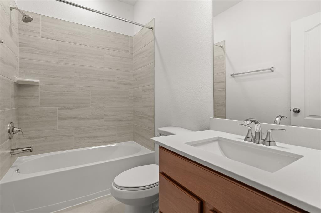 Primary bath features tile flooring, bath/shower combo with tile surround, wood cabinets, beautiful light countertops, mirror, sleek fixtures and modern finishes!