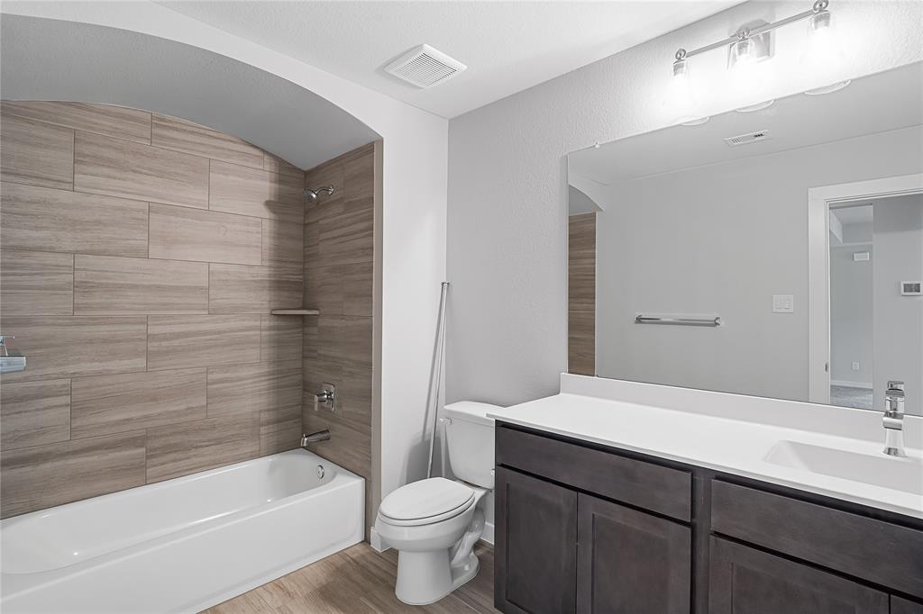 Secondary bath features tile flooring, bath/shower combo with tile surround, dark wood cabinets, beautiful light countertops, mirror, sleek fixtures and modern finishes