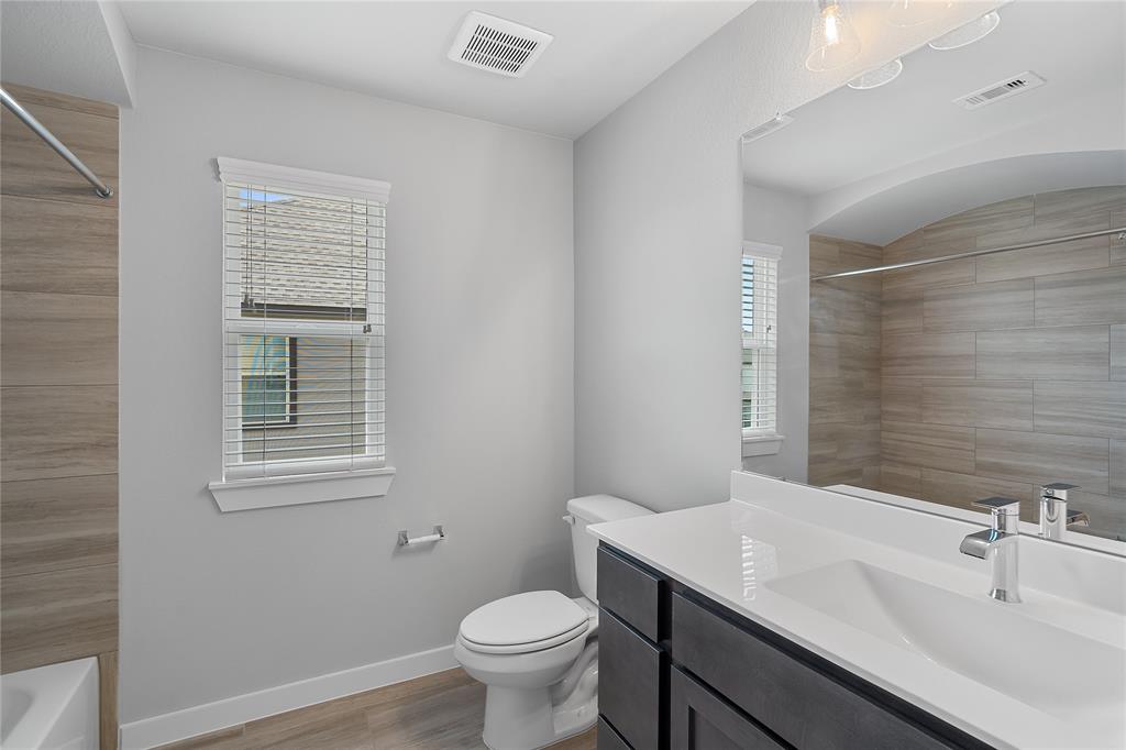 Secondary bath features tile flooring, bath/shower combo with tile surround, dark wood cabinets, beautiful light countertops, mirror, sleek fixtures and modern finishes