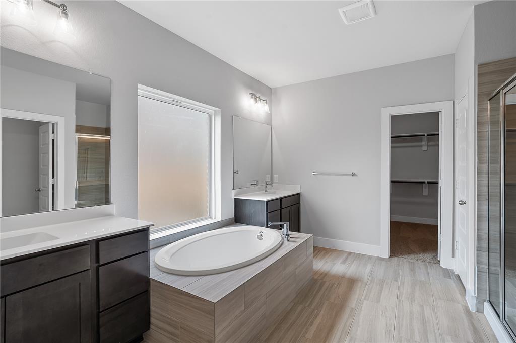 This primary bathroom is definitely move-in ready! Featuring an oversized walk-in shower with tile surround, separate garden tub for soaking after a long day with custom tile detailing, dark stained cabinets with light countertops, spacious walk-in closet with shelving, high ceilings, neutral paint, sleek and modern finishes.