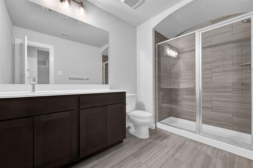 Secondary bath features tile flooring, walk in shower with tile surround, dark wood cabinets, beautiful light countertops, mirror, sleek fixtures and modern finishes.