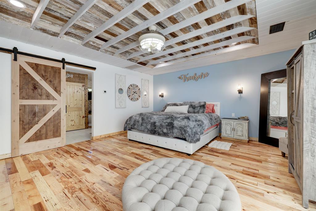 Another view of the Primary en suite, notice the drop down ceiling fans in all the rooms, window treatments throughout and custom shiplap accent ceiling. Barndoor leads to the primary en suite bathroom.