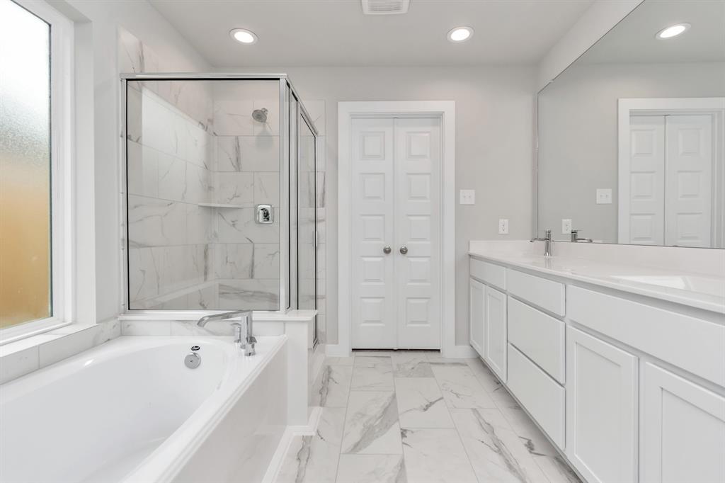 Enjoy a walk-in shower with tile surround, a separate garden tub with custom detailing, and an elegant vanity featuring light countertops, modern hardware, and bright recessed lights. Experience luxury and relaxation in every detail