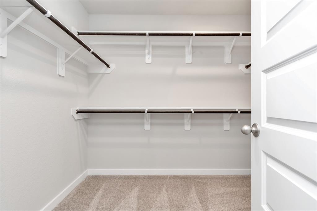 Experience luxury in this spacious walk-in closet with high ceilings and plush carpet. Warm paint tones, built-in shelving, and dark finishes create a contemporary and functional retreat