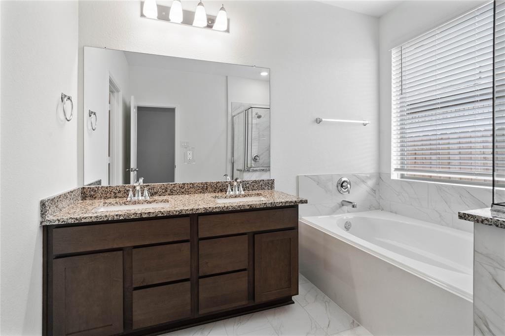 This primary bathroom is definitely move-in ready! Featuring a walk-in shower with tile surround, separate garden tub for soaking after a long day with custom tile detailing, stained cabinets with granite countertops, high ceilings, neutral paint, sleek and modern finishes.