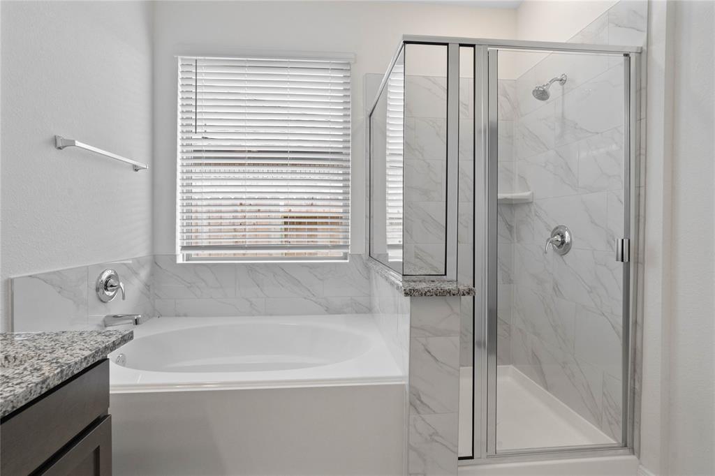 This primary bathroom is definitely move-in ready! Featuring a walk-in shower with tile surround, separate garden tub for soaking after a long day with custom tile detailing, stained cabinets with granite countertops, high ceilings, neutral paint, sleek and modern finishes.