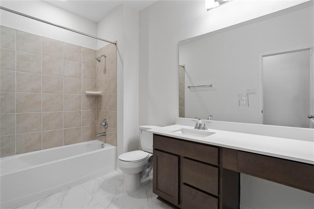 Secondary bath features tile flooring, bath/shower combo with tile surround, wood cabinets, beautiful light countertops, mirror, sleek fixtures and modern finishes.