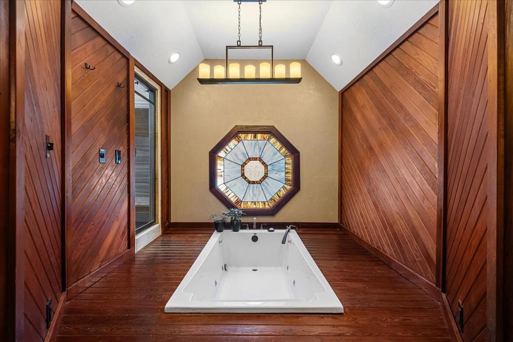 The raised oversized soaking tub is a luxurious centerpiece, set amidst a wooden deck reminiscent of a spa retreat. The warm wood tones complement the natural light filtering through the stained glass window, casting a colorful and serene ambiance over the tub. The deck creats a tranquil oasis where one can unwind and rejuvenate in the comfort of their own home.