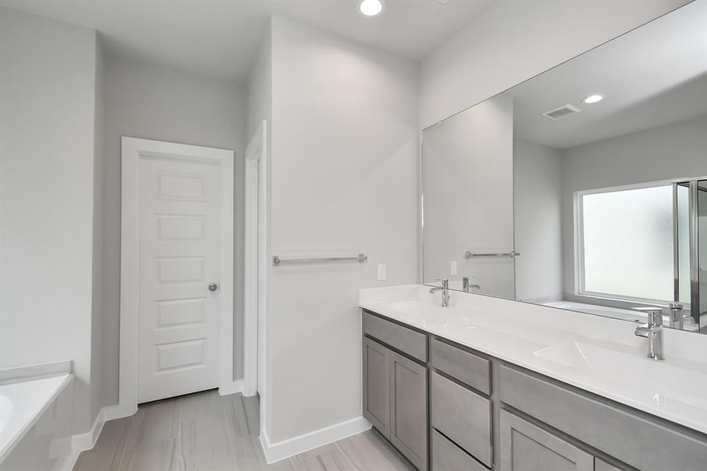 Enhance your daily rituals at the sophisticated vanity, featuring double sinks, light-colored countertops, contemporary hardware, and bright recessed lights.