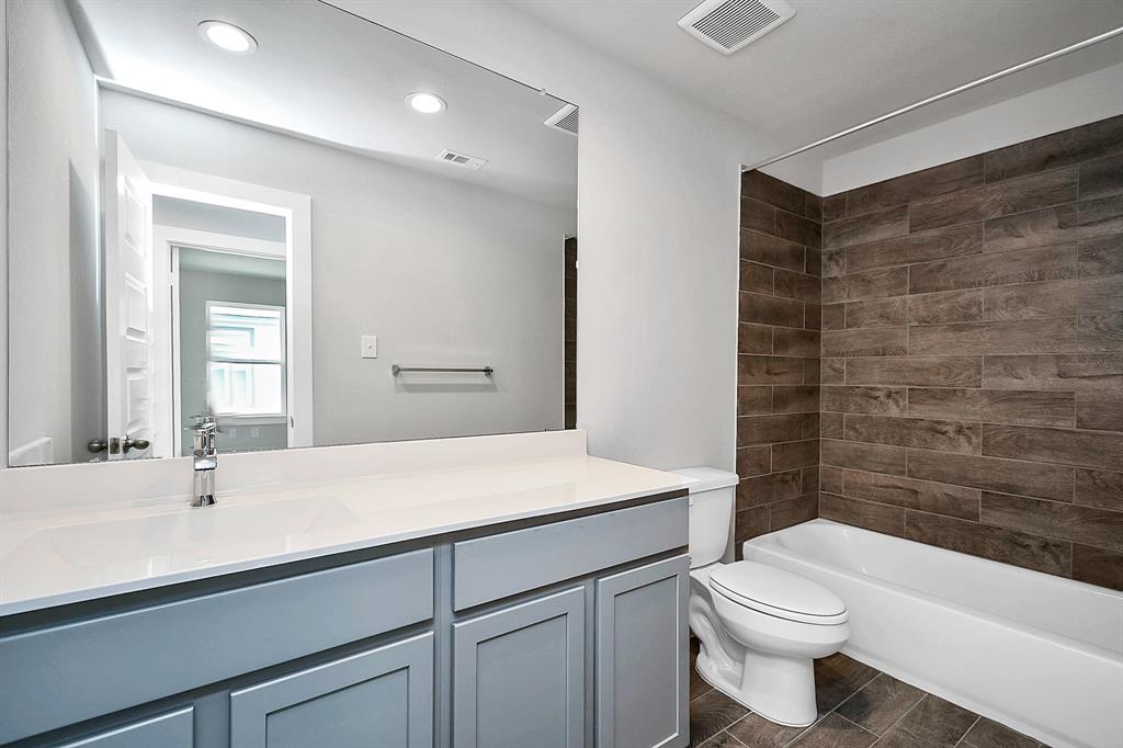 Secondary bath features tile flooring, bath/shower combo with tile surround, light stained wood cabinets, beautiful light countertop.