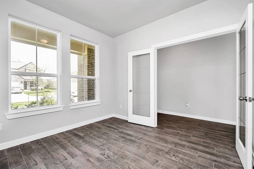 Experience the perfect blend of sophistication and warmth in this home office, boasting elegant wood-look tile flooring and flooded with natural light from expansive windows and French doors