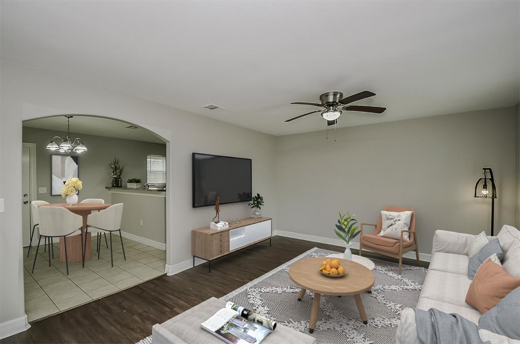 Living room virtually staged with a gray sectional sofa, patterned rug, laminate floors, and a staircase leading upstairs.