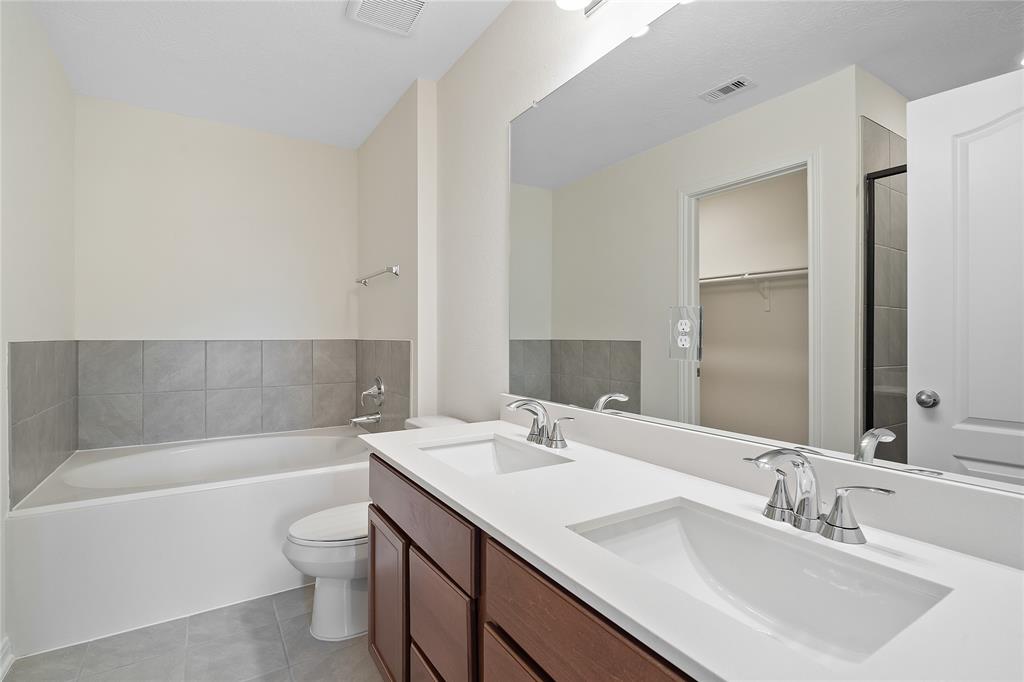 This primary bathroom is definitely move-in ready! Featuring a walk-in shower with tile surround, light stained cabinets with light countertops, spacious walk-in closet with shelving, high ceilings, custom paint, sleek and dark modern finishes.