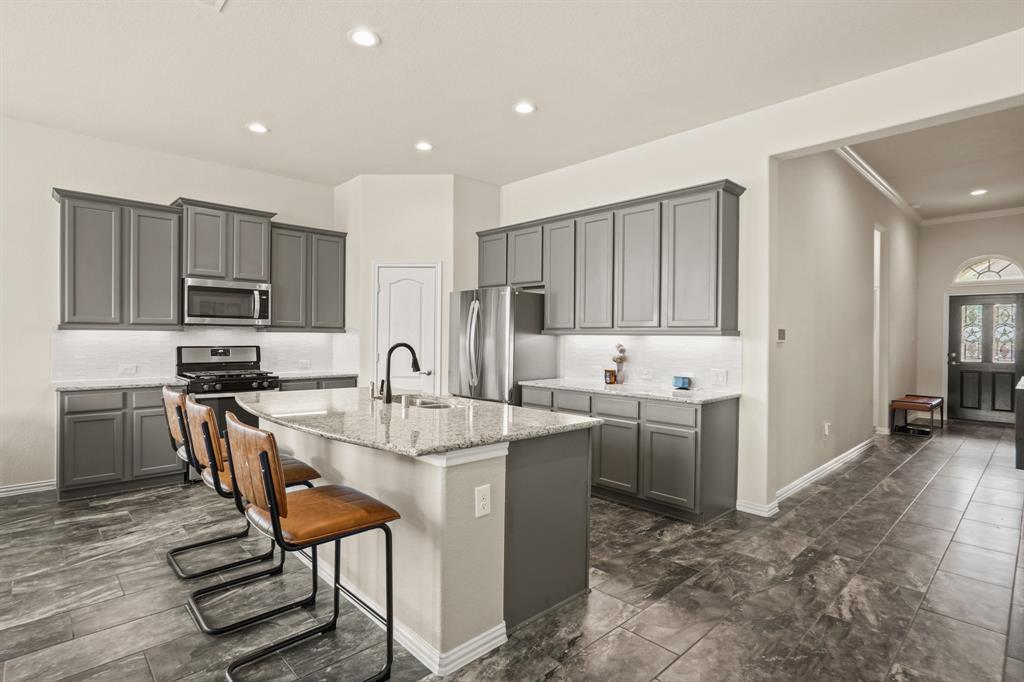 Elevate your culinary experience in this Chef\'s island kitchen, adorned with stylish gray cabinets with under cabinet lighting, and elegant granite counters with a sleek white backsplash.