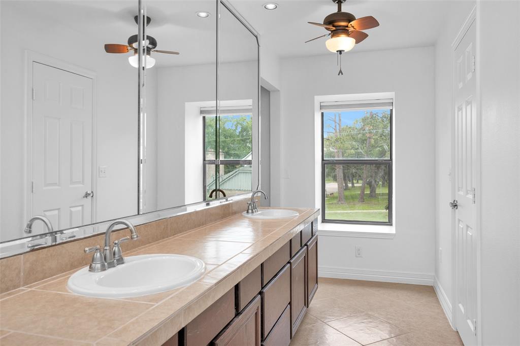 Primary Bath offers wonderful dual sinks, tile countertops, a ceiling fan & window allowing natural light to stream through.