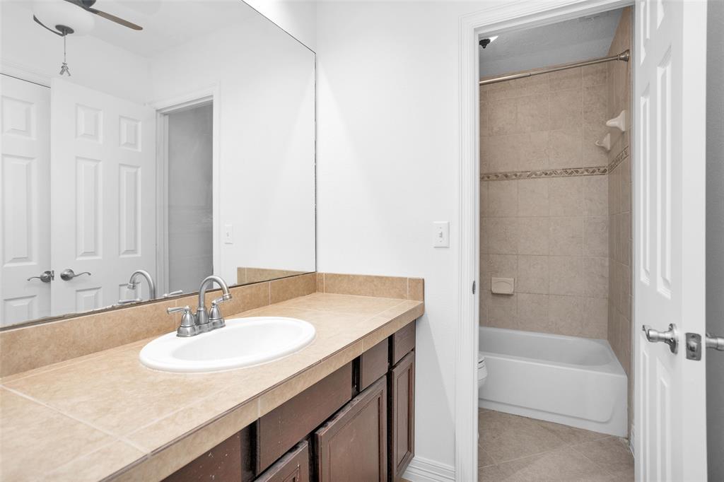 Crisp & clean Upstairs Secondary Bathroom w/ neutral colors, tile countertops, ceiling fan to keep cool, & a private shower/toilet area.