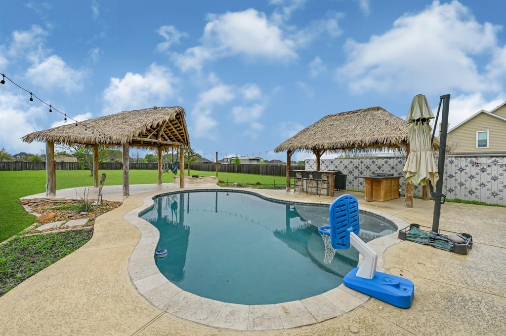 This backyard oasis features swimming pool with sun deck, covered cabana area equipped with electric and water taps, outdoor kitchen, gas fire pit and access to over an acre of fenced yard space.