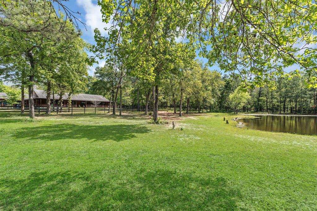 Unrestricted, stunning, and 15.01 acres just outside of Mill Creek subdivision featuring a stocked pond, deer stand, 6 stall horse barn with electric/water, storage room, BBQ pit, and shipping container!  Water pipes have been run to pond so you can install a water feature. Custom log cabin with front door facing west on double slab per seller with wraparound porch facing pond!  Porch alone is a grand 2264 SF!  Home is on aerobic system.  Home features granite countertops, beautiful wood flooring/trim, 2 water heaters, 2 ac's, R/W/D included and open floorplan!  Primary suite is spacious and airy. Home is a 5 bedroom with a flex space intended for mud room but currently used as an exercise room.  Mobile home on property can be used for extra living quarters and has its own septic.  Property is close to all amenities, Tomball and The Woodlands, but still manages to make you feel as if you have escaped the hustle and bustle!  Serenity at its finest lies just beyond the electronic gate!