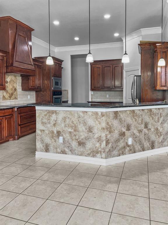 Kitchen featuring pendant lighting, ornamental molding, appliances with stainless steel finishes, custom range hood, and tasteful backsplash