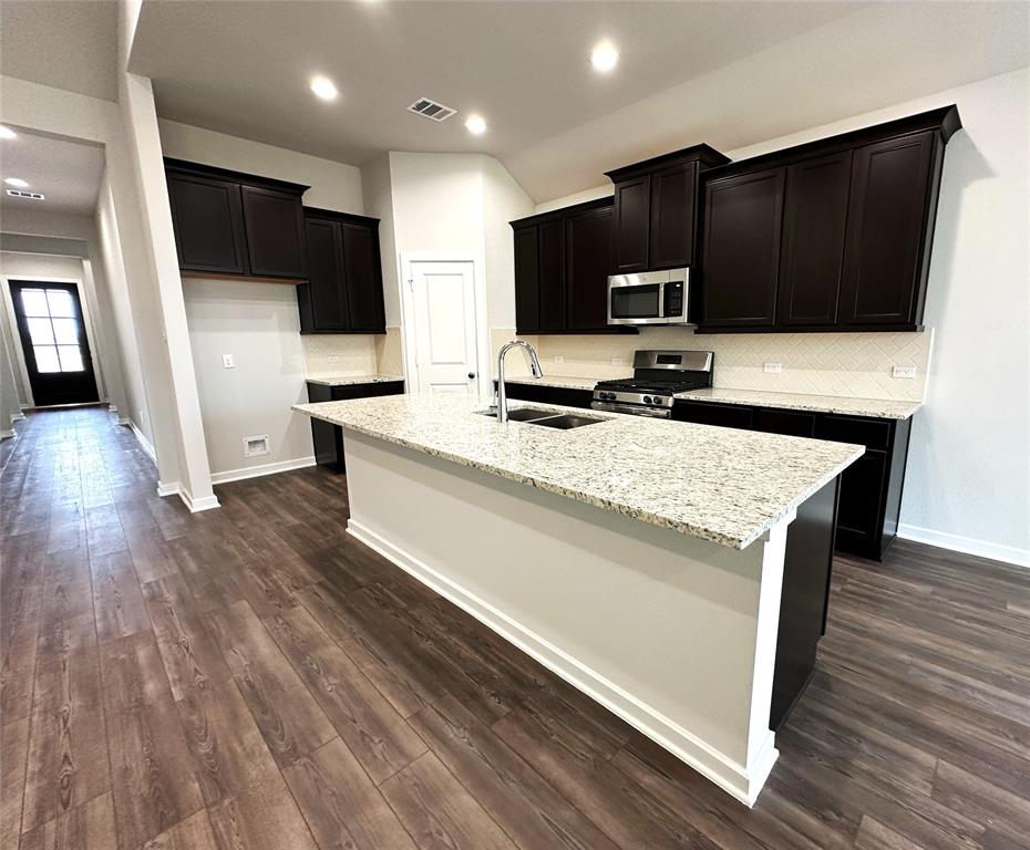 View of kitchen towards front door- corner walk in pantry-gas cooktop- granite- subway tile