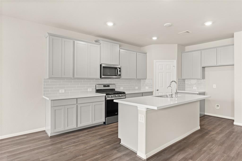 This light and bright kitchen features a large quartz island, white cabinets, a large sink overlooking your family room, recessed lighting, and beautiful backsplash.