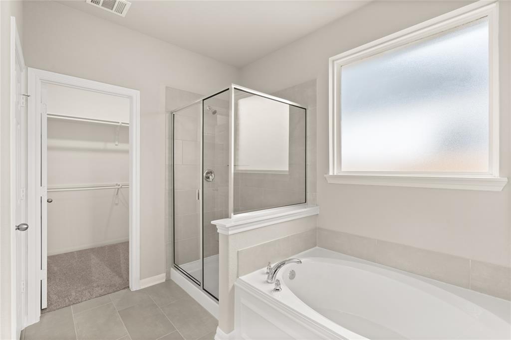 This additional view of your primary bathroom features tile flooring, fresh paint, walk-in shower, a separate garden tub, and a large walk-in closet.