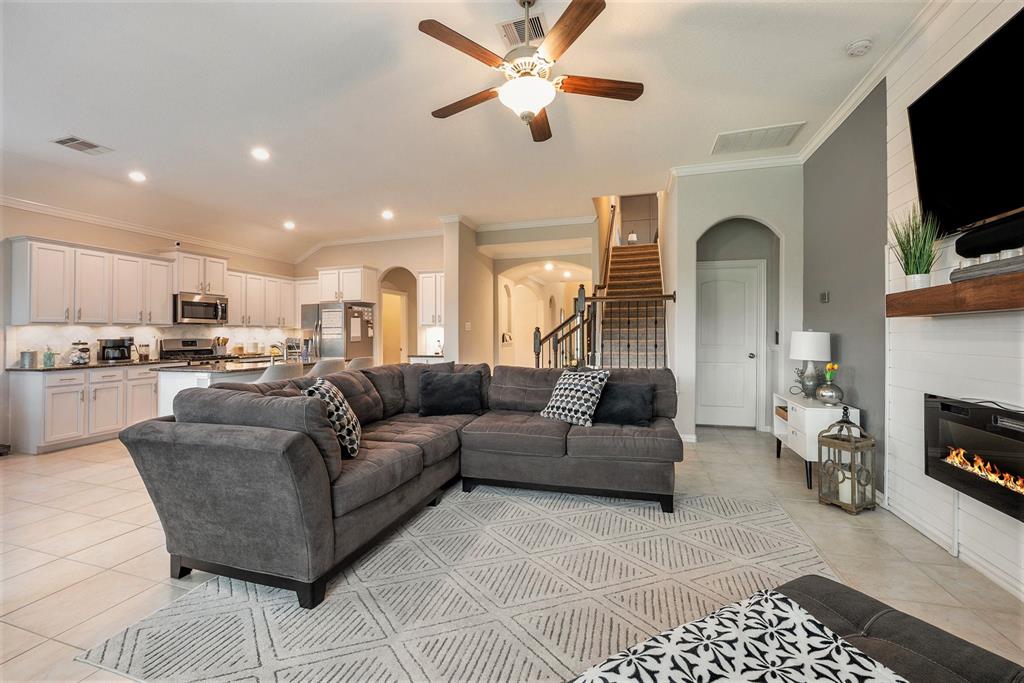 A modern, open-concept living room with a sectional sofa, kitchen in the background, a fireplace, and a staircase leading to an upper level.