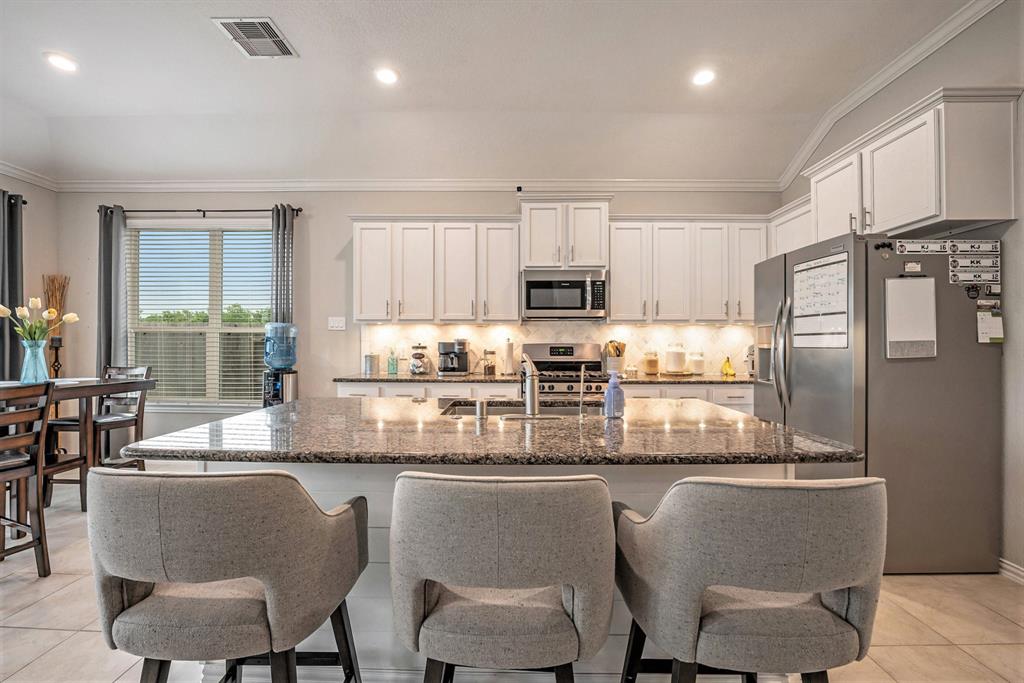 Modern kitchen interior with granite island, stainless steel appliances, white cabinetry, and bar stools. Bright and clean design.