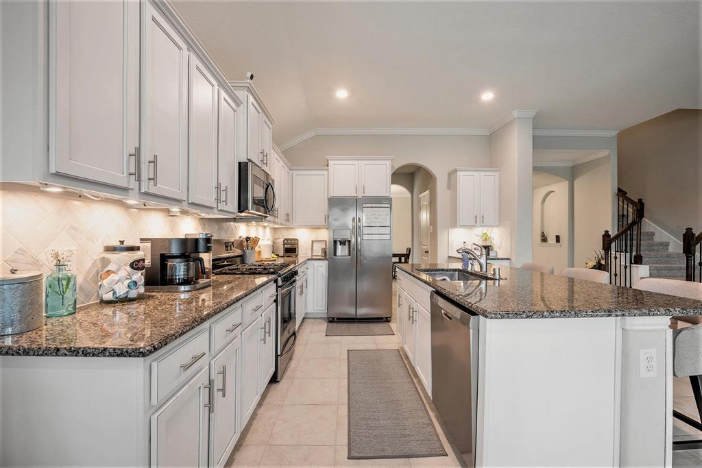 Modern kitchen interior with granite countertops, stainless steel appliances, white cabinetry, and a central island with seating.