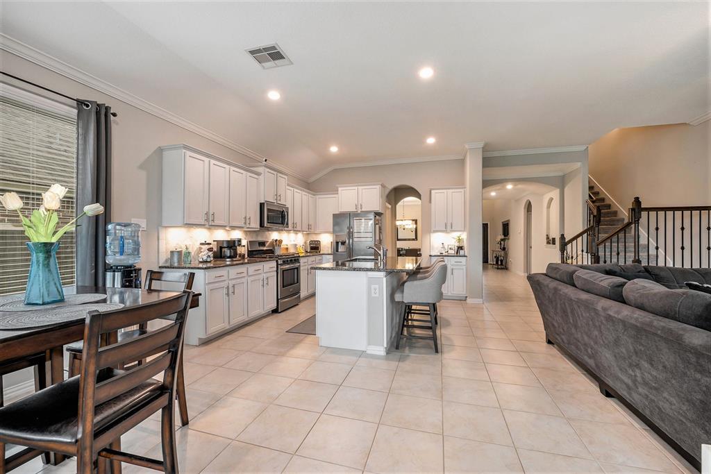 Modern kitchen with white cabinets, stainless steel appliances, and an island, opening to a living area with a large sofa and staircase.