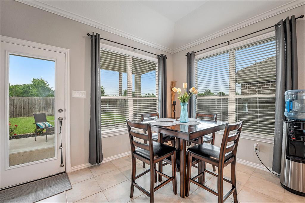 Bright dining nook with a round table, four chairs, large windows, a water cooler, and a view of a backyard through a glass door.