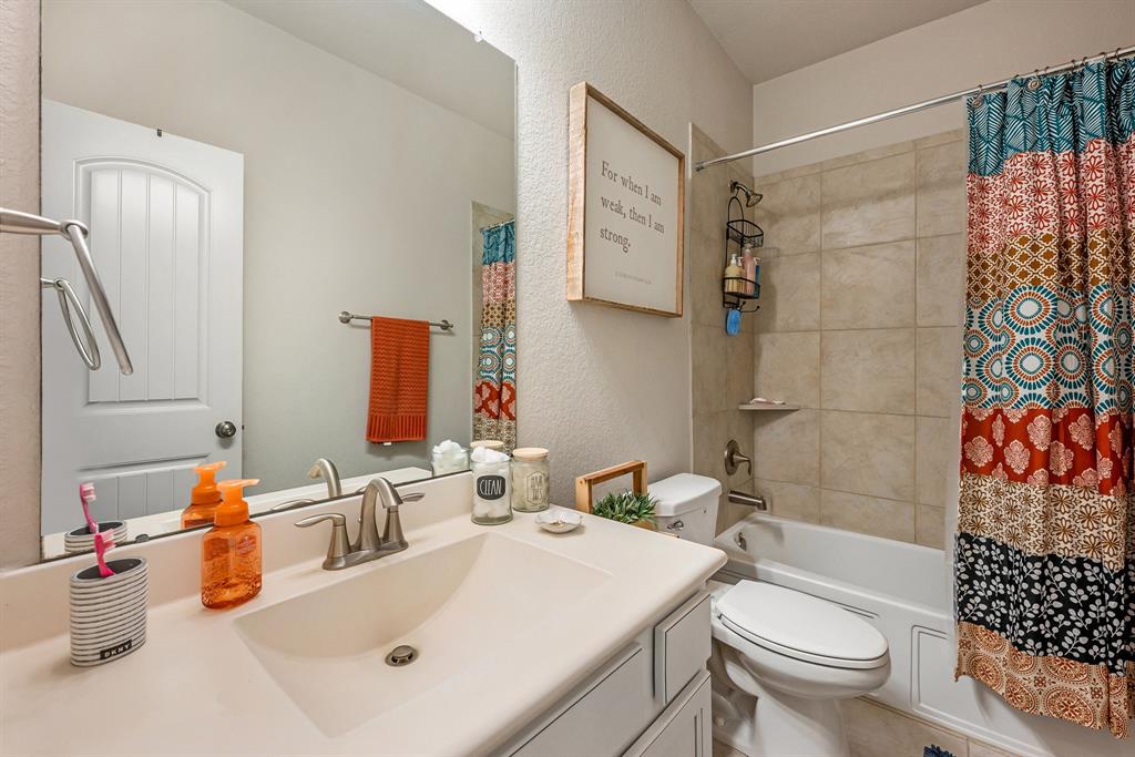 A clean downstairs guest bathroom with a patterned shower curtain, beige tiles, and decorative accents like a framed quote and colorful towels.