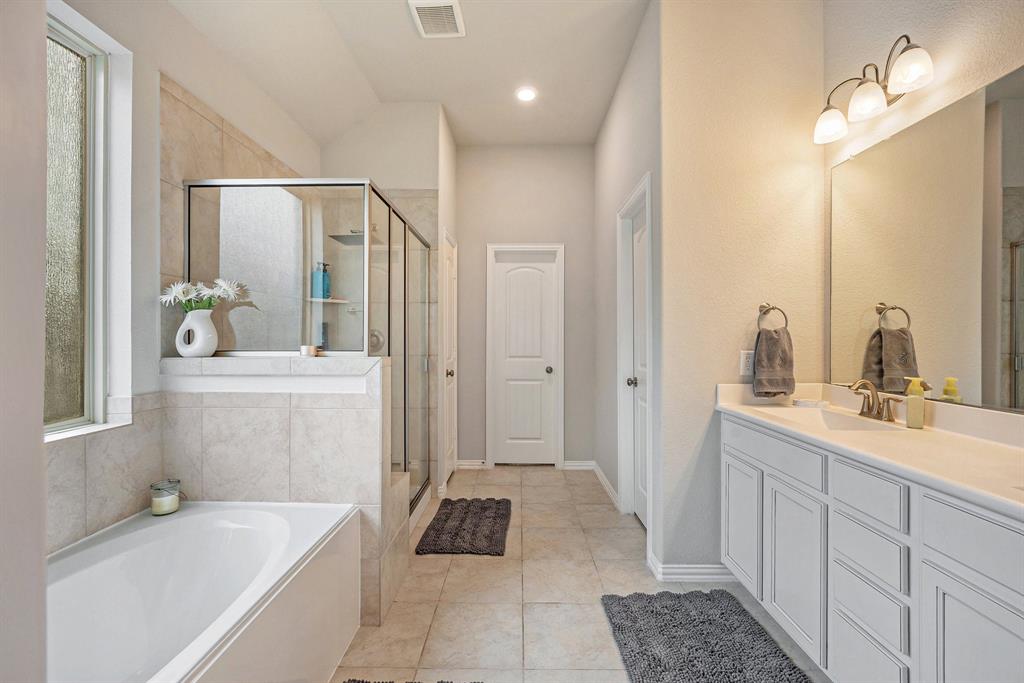 A modern primary bathroom with a dual sink vanity, large mirror, glass shower, and a bathtub, decorated in neutral tones with natural light.