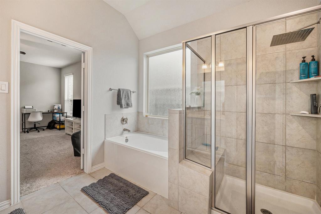 Modern primary bathroom with a glass-enclosed shower, bathtub, tiled walls, and a view into an adjoining room with a desk and computer.