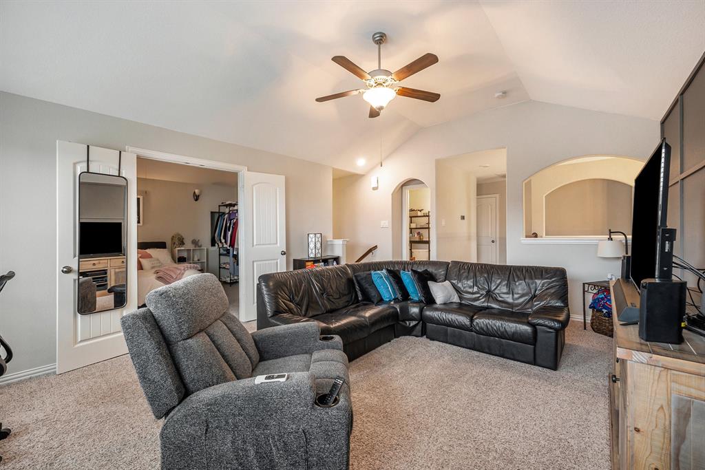 A spacious upstairs game room with a black leather sectional sofa, grey recliner, and visible bedroom entrance in a modern home interior.