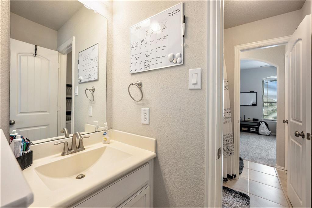 A clean, well-lit bathroom with a sink, mirror, and white cabinets, featuring decorative elements and a view into an adjoining room.