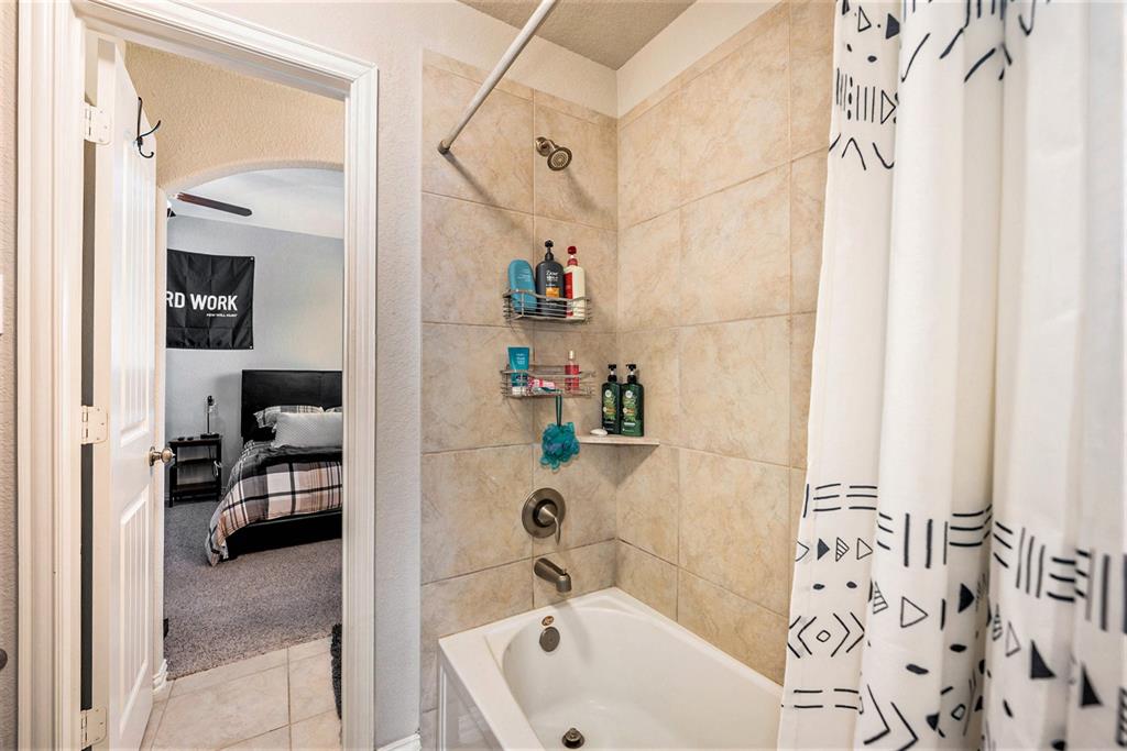 A bathroom with a shower curtain, visible toiletries, and a view into a bedroom.