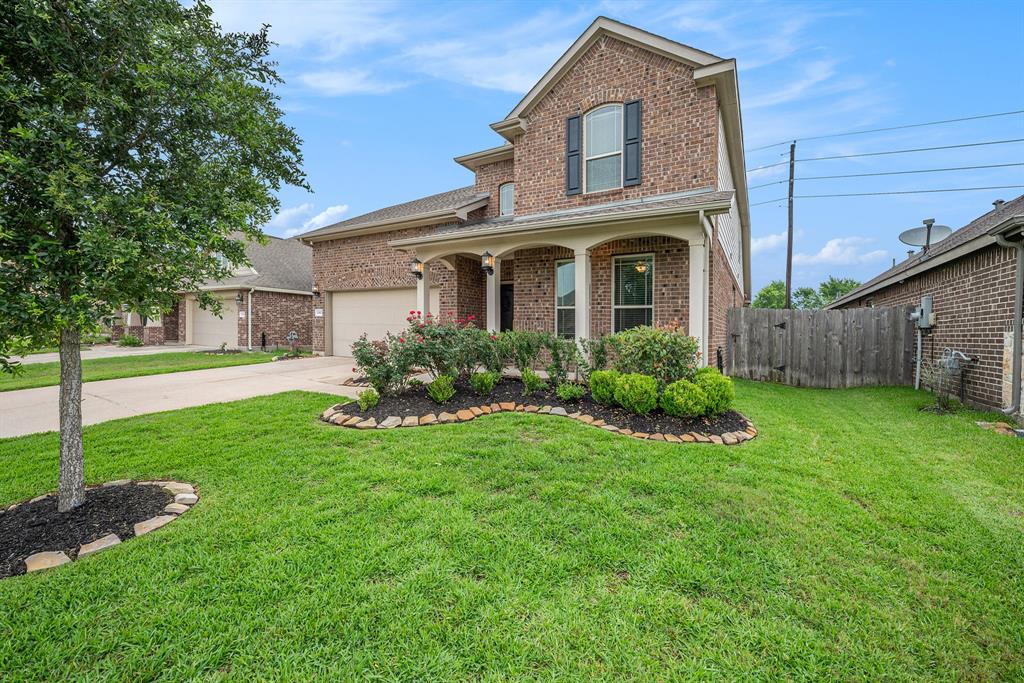 Two-story brick house with landscaped front yard, curved pathway, and a well-maintained lawn under a cloudy sky.