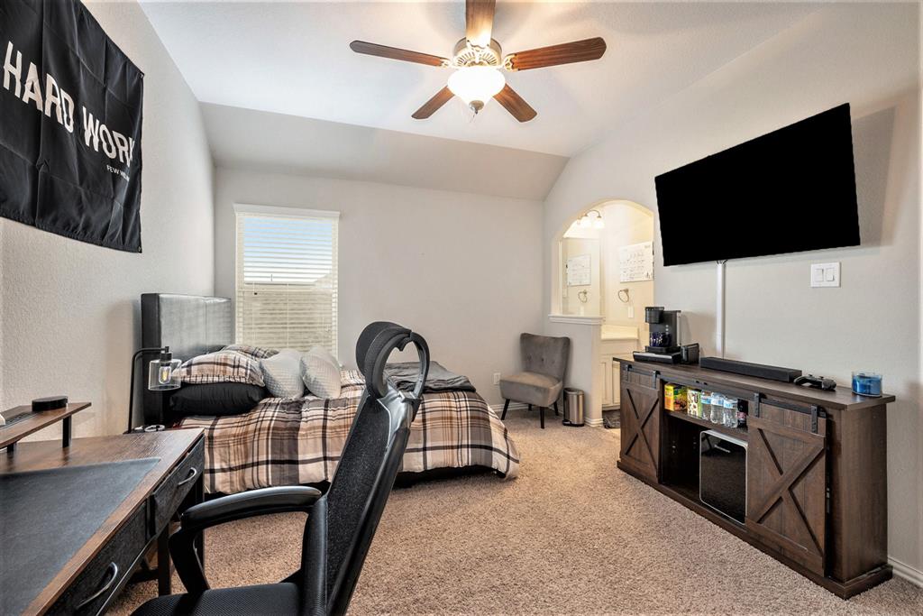 Modern bedroom with a large bed, desk, gaming chair, TV, and motivational banner. Neat and organized with a neutral color scheme.