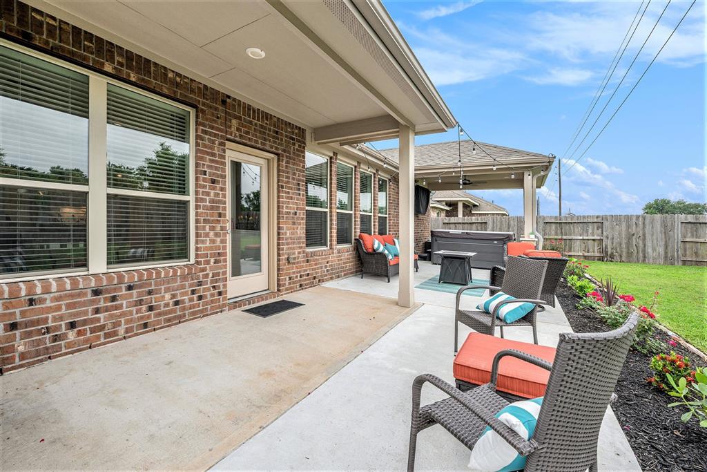 A cozy backyard patio with comfortable furniture, a grill, and vibrant plants, adjoining a brick house under a clear sky.