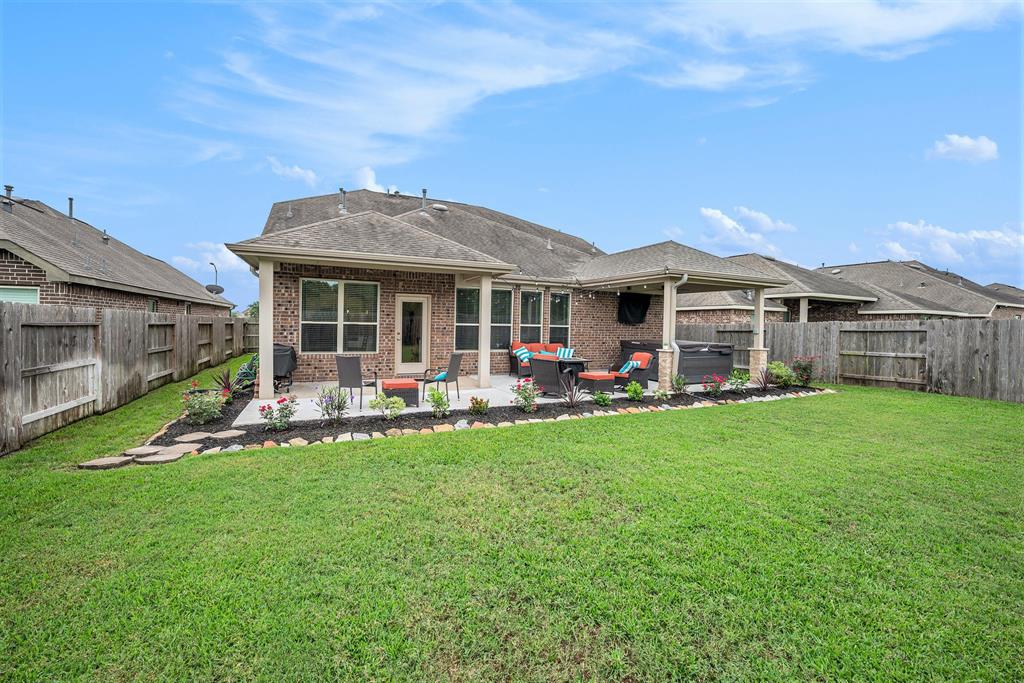 A well-maintained backyard with a patio area, lawn chairs, vibrant flowerbeds, and a wooden fence under a clear sky.