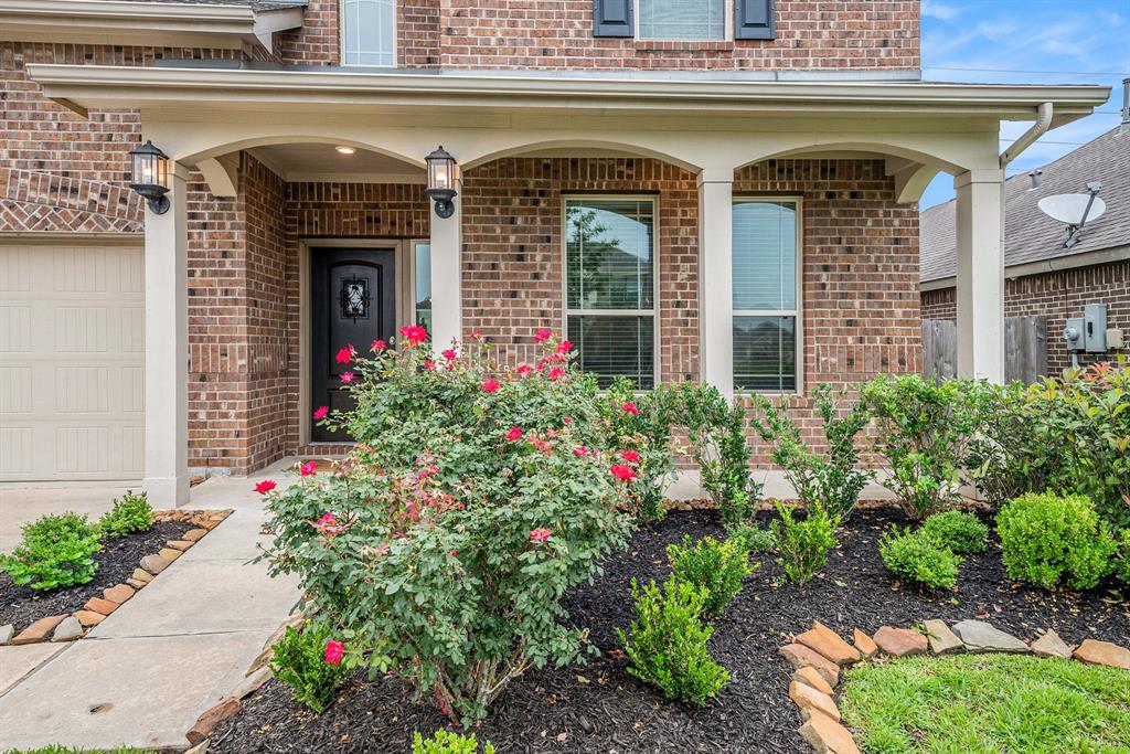 A brick house entrance with a landscaped garden featuring red roses and green shrubs.